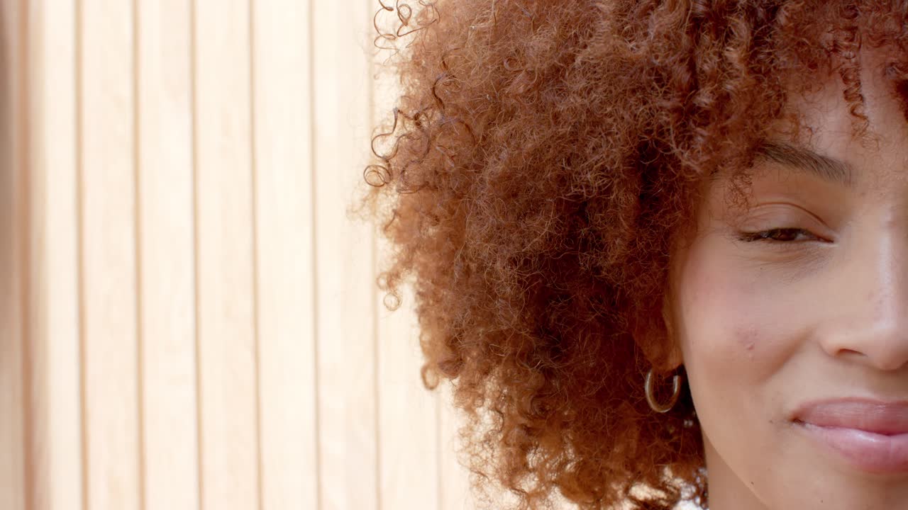 Adult woman wearing silver hoops holding gaze against sunlit wood slats blinking, copy space