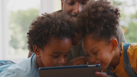 Padre-En-Casa-Con-Niños-Tumbados-En-Una-Alfombra-Jugando-Con-Una-Tableta-Digital