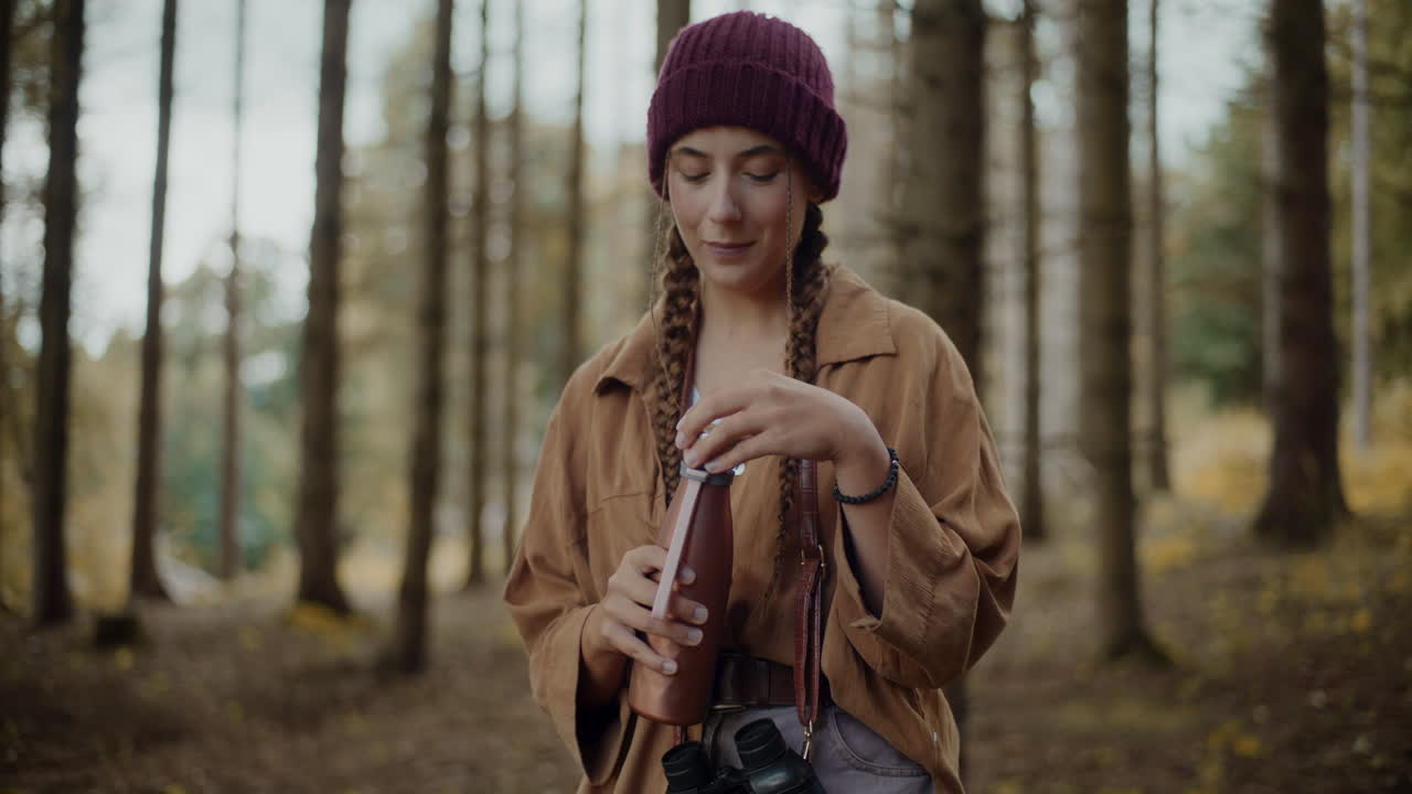 туристка открывает крышку бутылки в лесу.