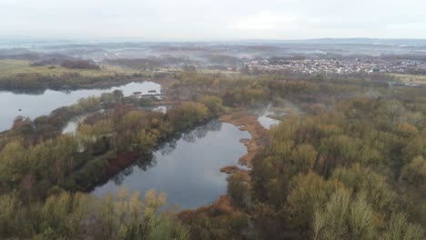 Foggy-dawn-misty-colourful-nature-reserve-autumn-woodland-landscape-aerial-pull-back