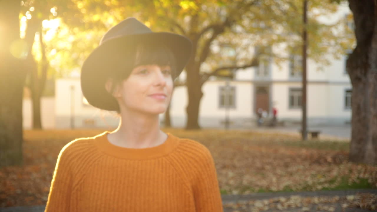 A young brunette woman walking under trees in Autumn, smiling in slow motion