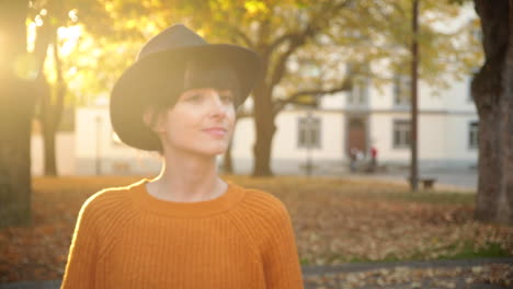 a young brunette woman walking under trees in autumn, smiling in slow motion