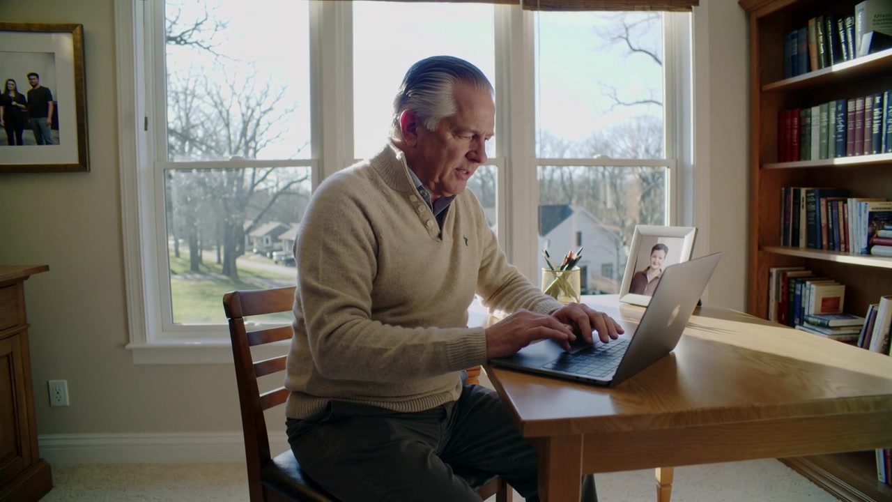 Typing senior man starting working on laptop at home study in beige sweater, handling tasks