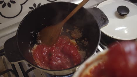 adding fresh tomato sauce into cooking hot pot on a gas stove