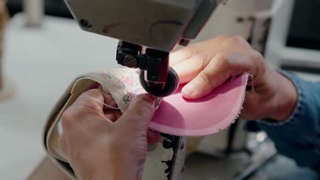 costurera de zapatos cosida de tela rosa con máquina industrial, primer plano de las manos en el trabajo