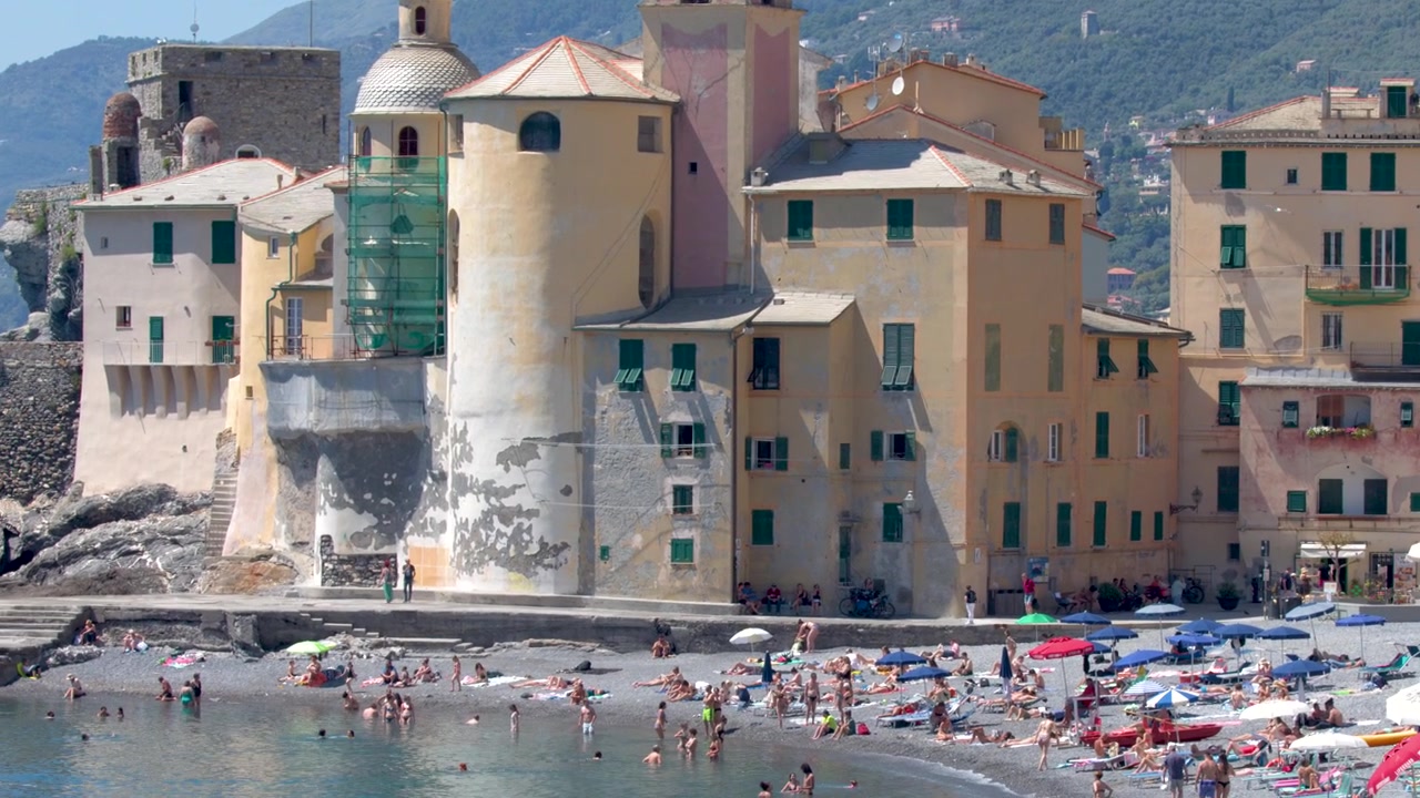 Una lenta panoramica rivela una vivace architettura costiera e una affollata spiaggia di ciottoli mediterranea