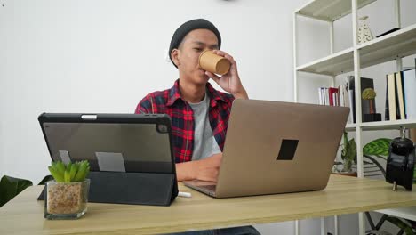 young asian man working from home on laptop and tablet