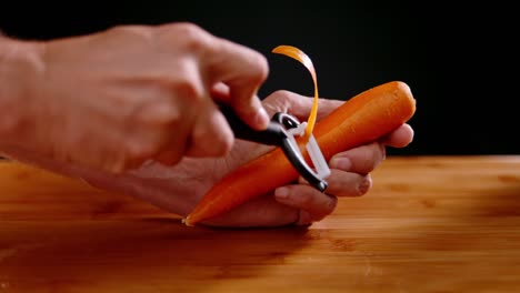 person hand peeling fresh orange carrot using peeling tool, slow motion view