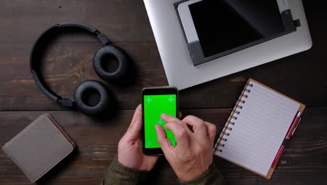 hands of man using smartphone with green screen on wood table