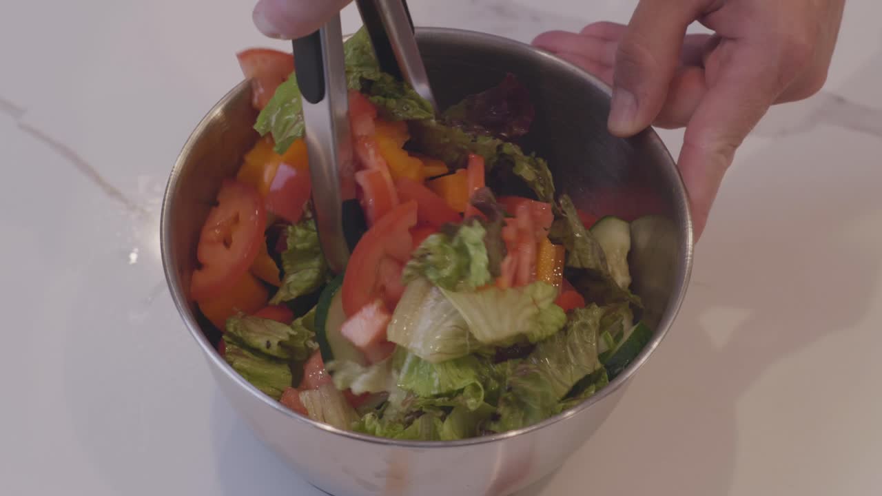 A slow motion close up of a fresh salad being mixed. Filled with lettuce, tomato, and yellow pepper