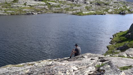 Person sitting on rock fishing in Norway mountain lake by himself before standing up and walking away