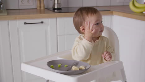 niña feliz sentada en una silla alta en la cocina, riendo y señalando algo durante la comida