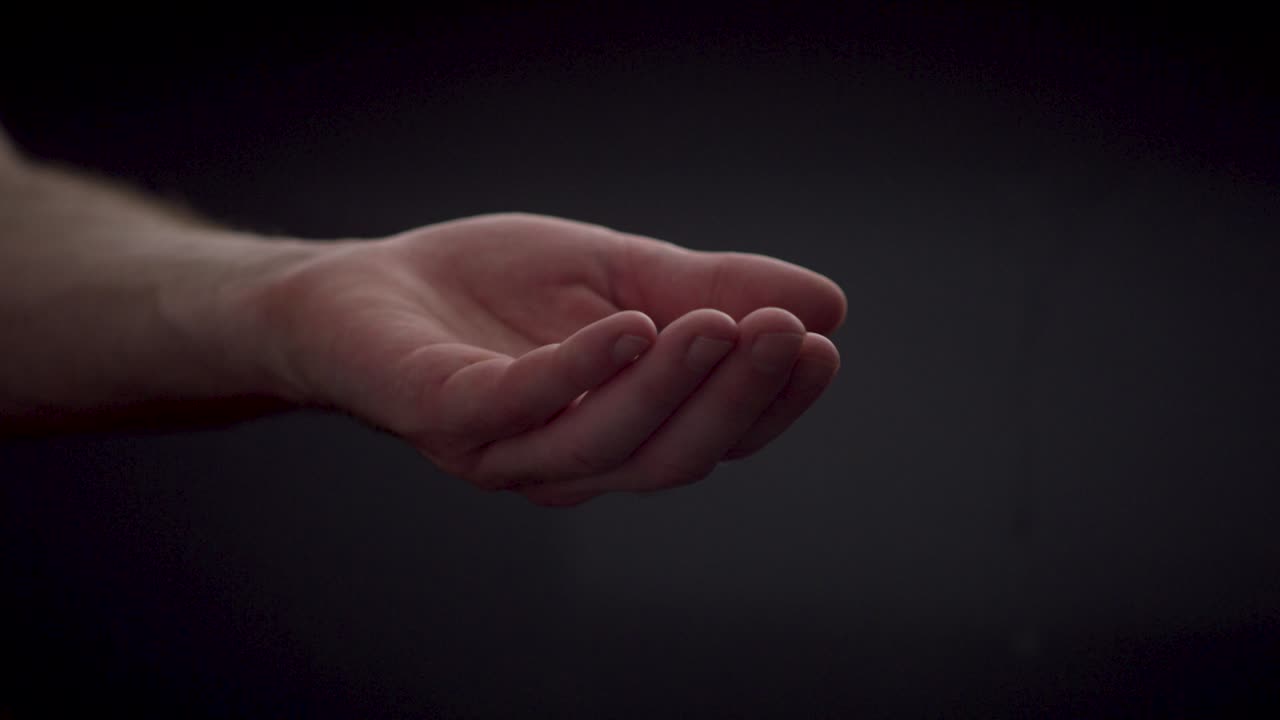 gotas de agua en cámara lenta cayendo en una mano caucásica abierta sobre un fondo negro