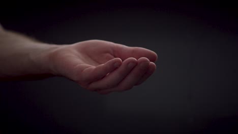 slow motion water droplets falling in open caucasian hand on black background