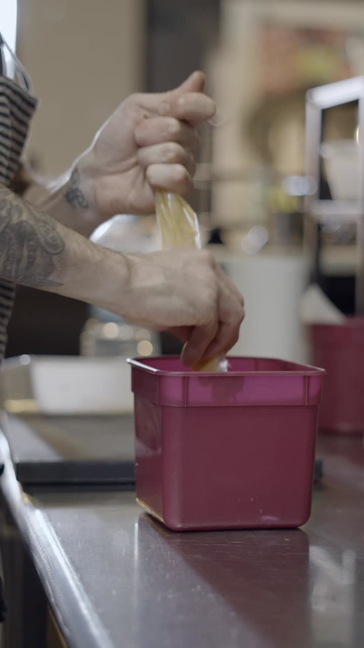 Hands squeezing food from a bag into a container in a kitchen