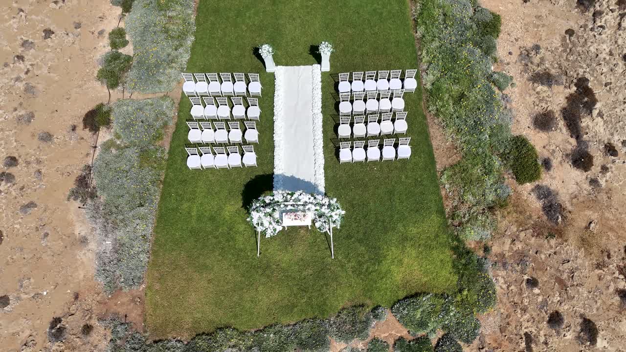 Un allestimento per un matrimonio in cui si vedono delle sedie bianche disposte ordinatamente sull'erba verde. Fiori e decorazioni incorniciano l'altare. La location è in un ambiente desertico.