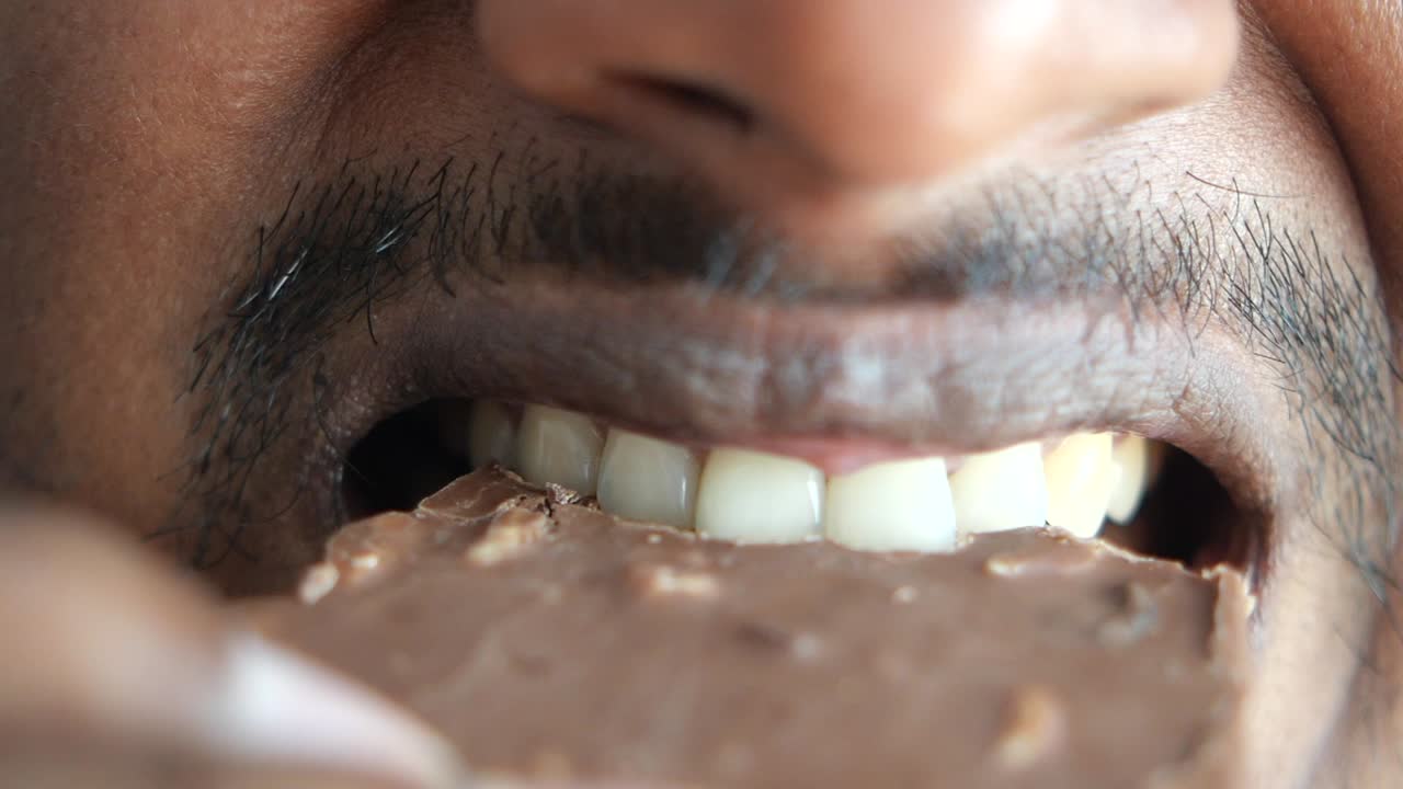 Close-up of a man's mouth eating chocolate