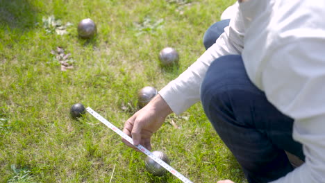 close-up beeld van een blanke jonge man die de afstand tussen petanqueballen in het park berekent