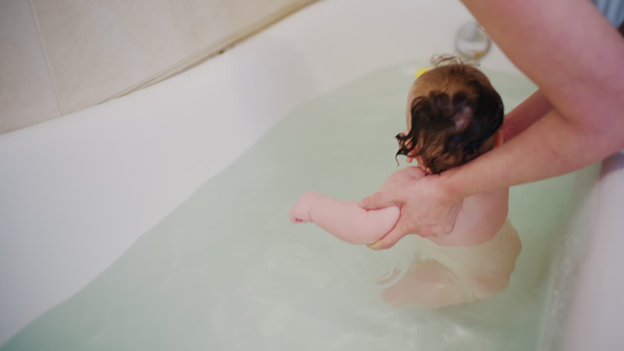 Parent supporting baby in bathtub while gently washing during bath time