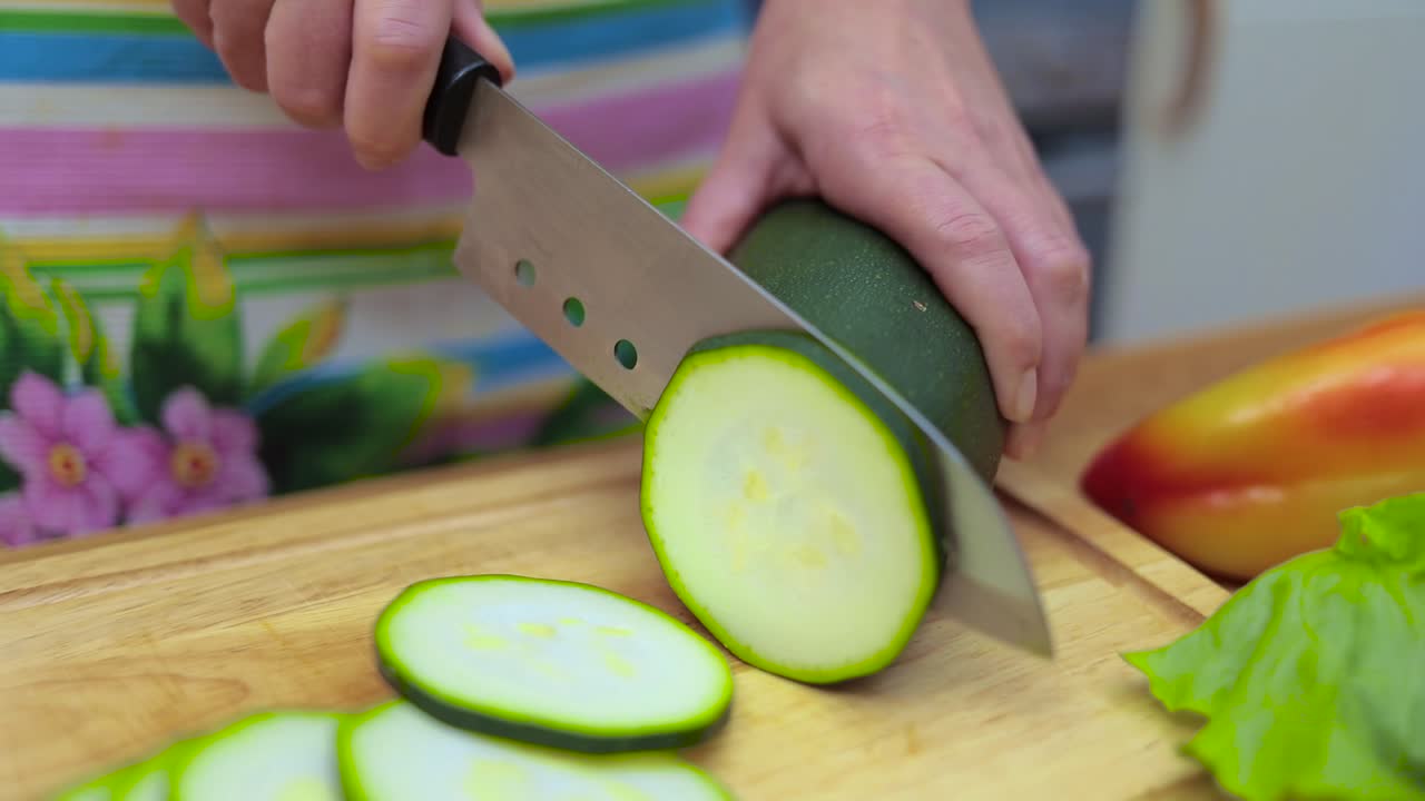 Women's hands Housewives cut with a knife fresh zucchini on the cutting Board of the kitchen table