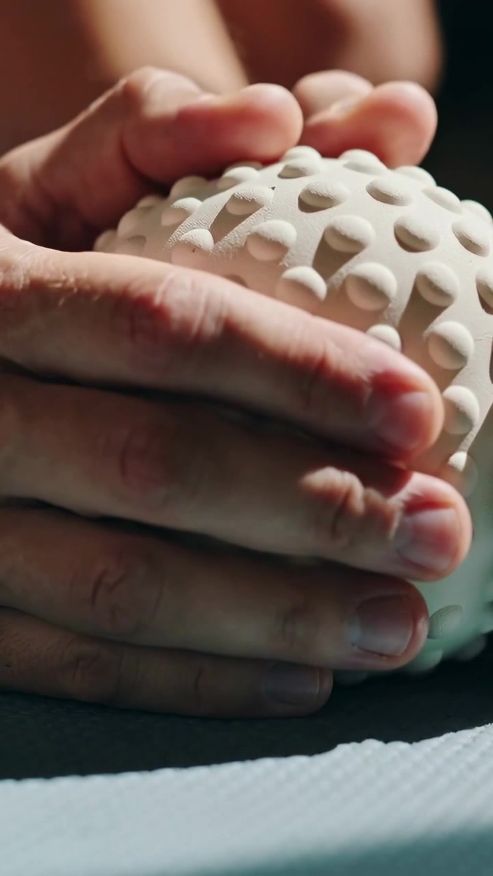 Vertical video: Cupping male hands manipulating white holed sphere on studio bench testing texture