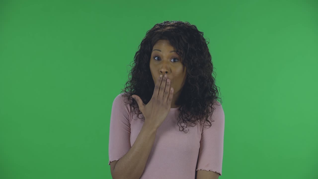 retrato de una hermosa mujer afroamericana joven confundida está mirando a la cámara diciendo oops y encogiéndose de hombros. bruneta ardiente con cabello ondulado en vaqueros y una blusa beige en una pantalla verde en el estudio