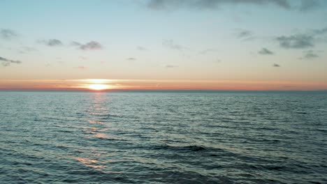 Drone-flying-over-calm-wavy-sea-at-sunset,-sunrise