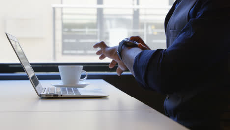 Mid-section-of-young-businessman-checking-his-smartwatch-while-working-on-laptop-at-desk-4k