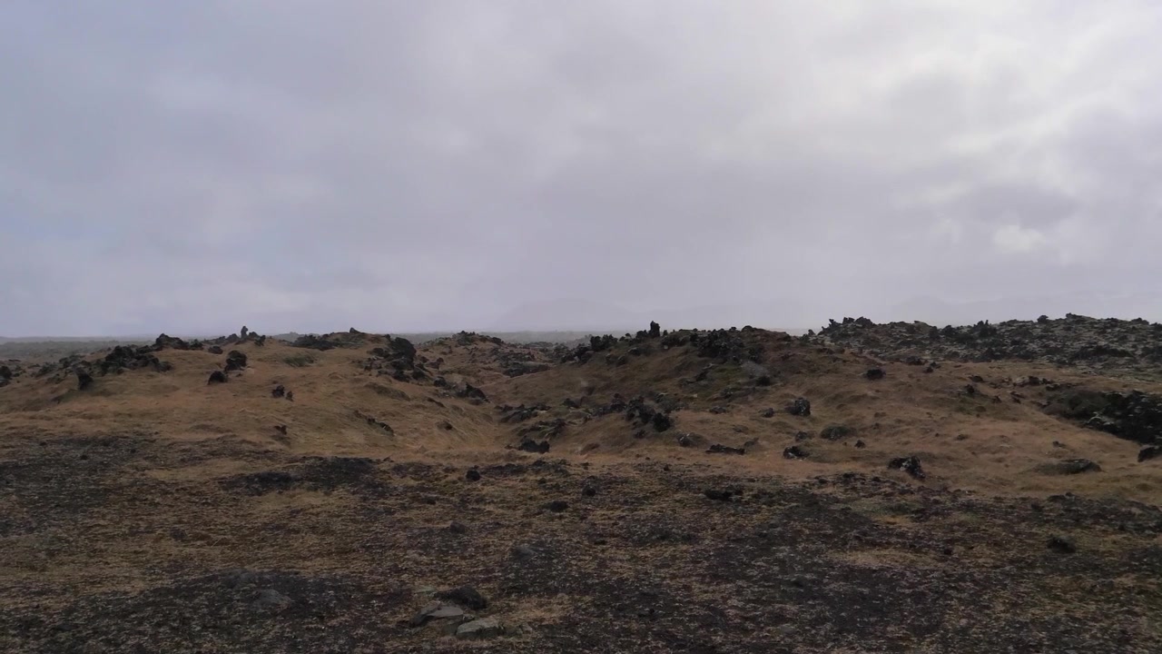 Volcanic highland landscape with dark rocks rugged ground and low overcast clouds across the open terrain in Iceland