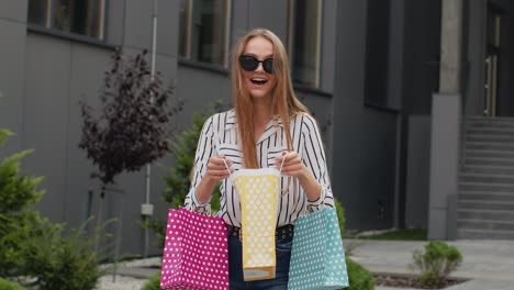 girl holding colorful shopping bags, rejoicing discounts in fashion store, enjoying shopping in mall