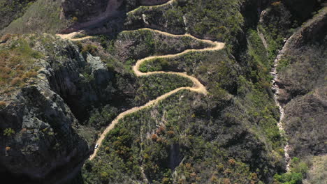 White-car-driving-down-winding-mountain-road,-top-down-tilt-up-aerial