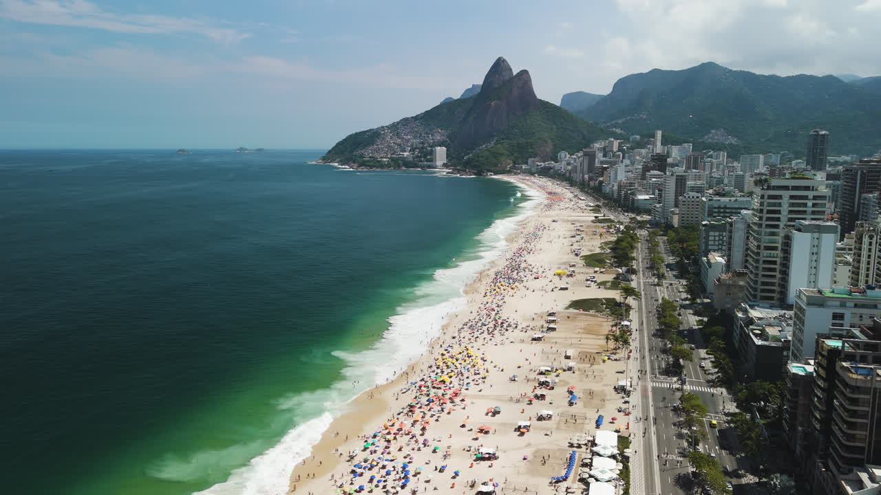 Drone descends over Ipanema Beach packed with umbrellas and joyful crowd in Rio de Janeiro