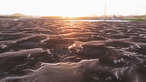 aerial dolly above warped mounds in asphalt lake at golden hour sunset, environmental damage