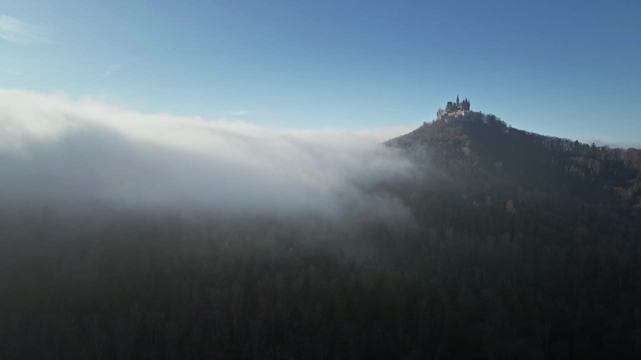 The drone soars forward towards the floating clouds, revealing the breathtaking landscape of Hohenzollern Castle, dense forests, and the vast German countryside.