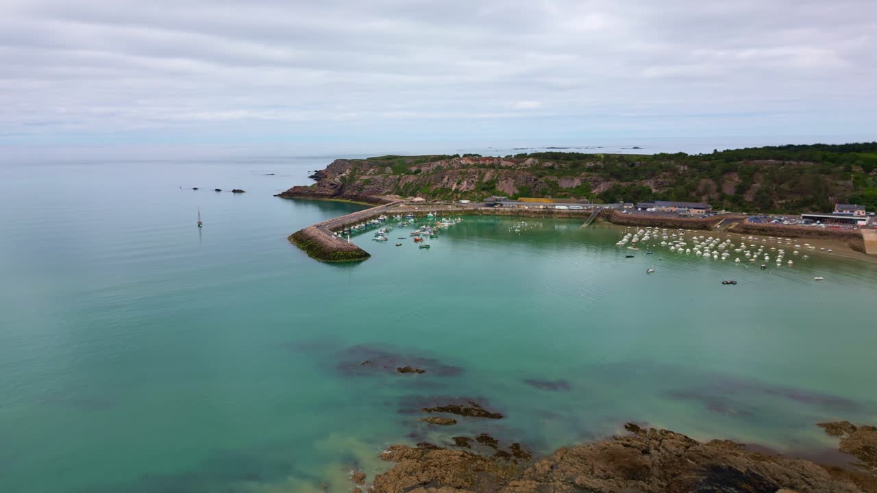 Sideways drone movement near a small harbor bay as a dock for local boats in cloudy day at Erquy, low tide, Côtes-d'Armor, Brittany, France.