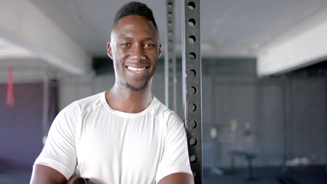 smiling man in gym wearing white shirt, leaning against metal pole