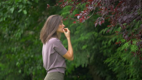 Beautiful cinematic shot of young woman reaching into cherry tree to pick fruit and eat it then smile at the camera in a lovely natural forest setting