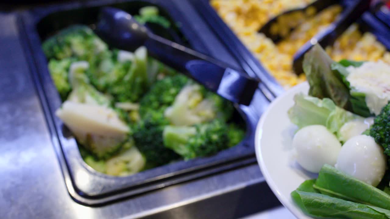 Primo piano di una donna che aggiunge verdure e mais a un piatto di insalata salutare a buffet