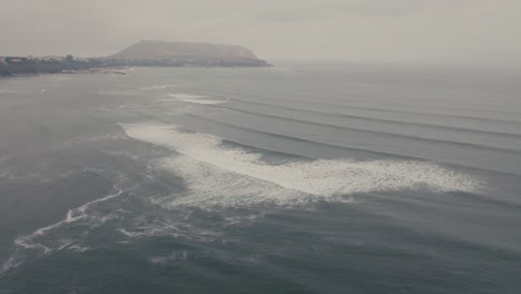 ocean waves rolling in a beach in peru on a cloudy day - aerial shot