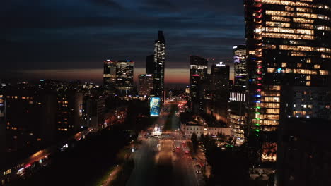 Night-city-scene,-High-rise-illuminated-buildings-along-wide-street.-Colourful-sunset-sky-in-background.-Warsaw,-Poland