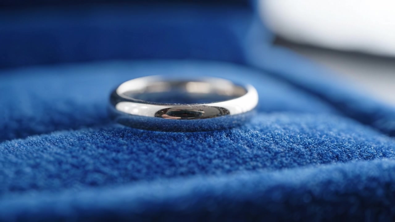 Cincin Perak Elegan Terletak di Bantal Beludru Biru Mewah, Menampilkan Kilau dan Keahlian yang Memukau, Sempurna untuk Melambangkan Cinta dan Komitmen