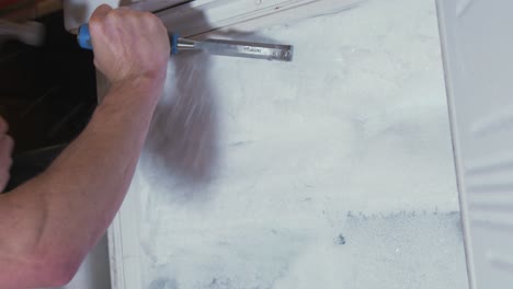 man chipping away ice from a frozen freezer