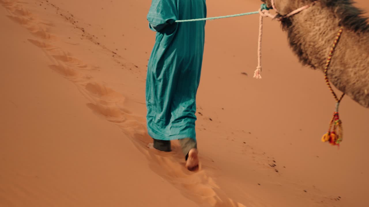 A traveler in blue robe walks barefoot, leaving footprints on Sahara sands in Morocco