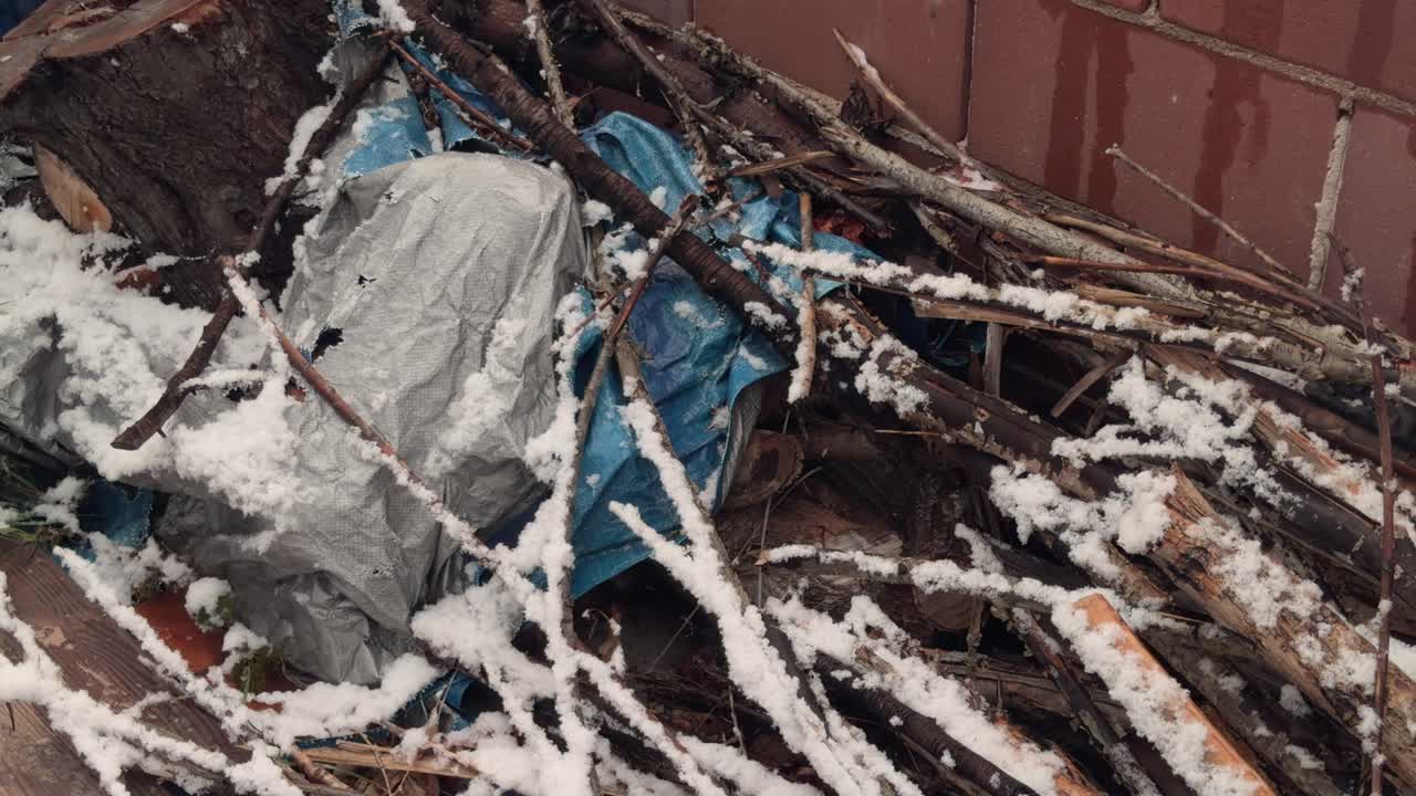Langsamer Schwenk über Brennholz und herabgefallene Äste, während draußen sanft Schnee fällt