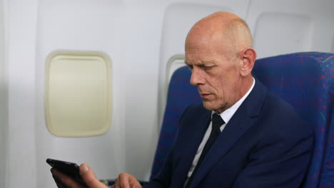 a mature business man working a tablet pc on an airliner airplane close up