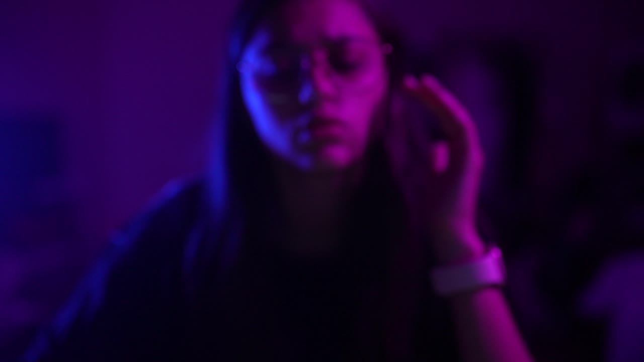 Primo piano di una giovane donna in felpa con cappuccio, con gli occhiali, sotto una vivace luce al neon viola e blu