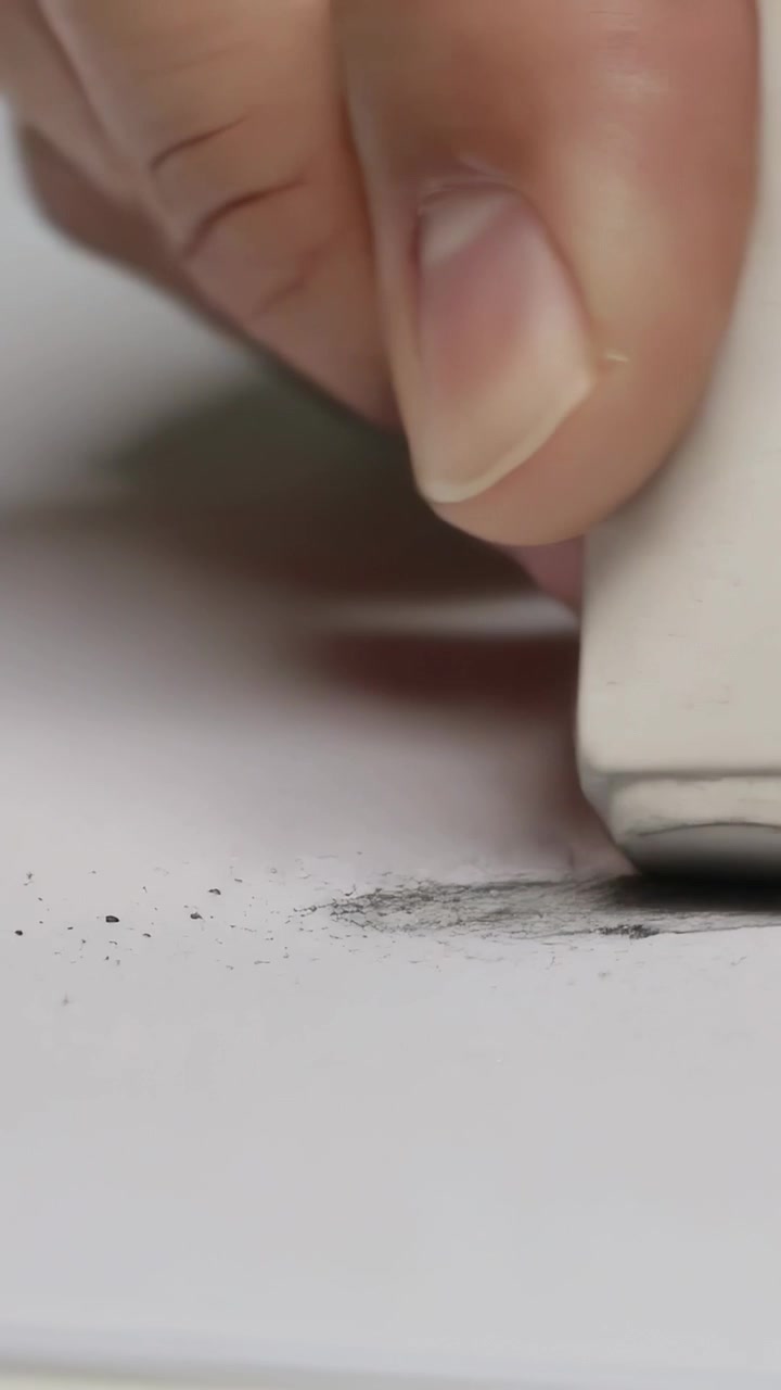 Vertical video: Placing right hand holding eraser onto pencil mark on paper, removing pencil mark