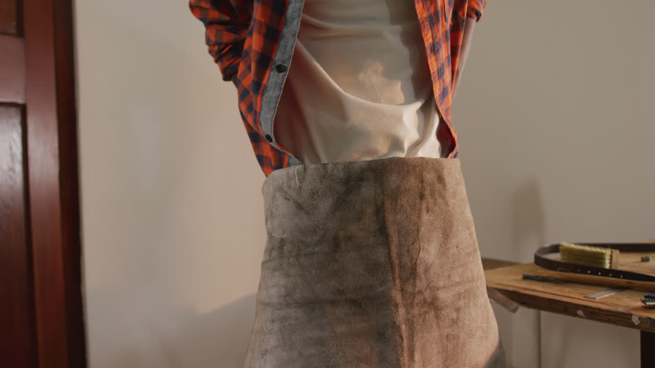 sección media de un artesano afroamericano que se pone un delantal en un taller de cuero