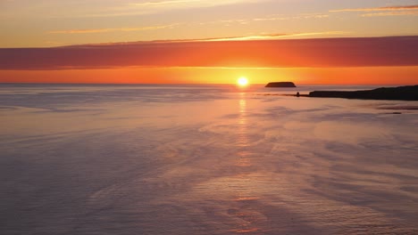 Beautiful-midnight-sunset-In-Iceland-at-ocean-coastline-shot-from-high-cliffs-with-rocks-silhouette-in-distance