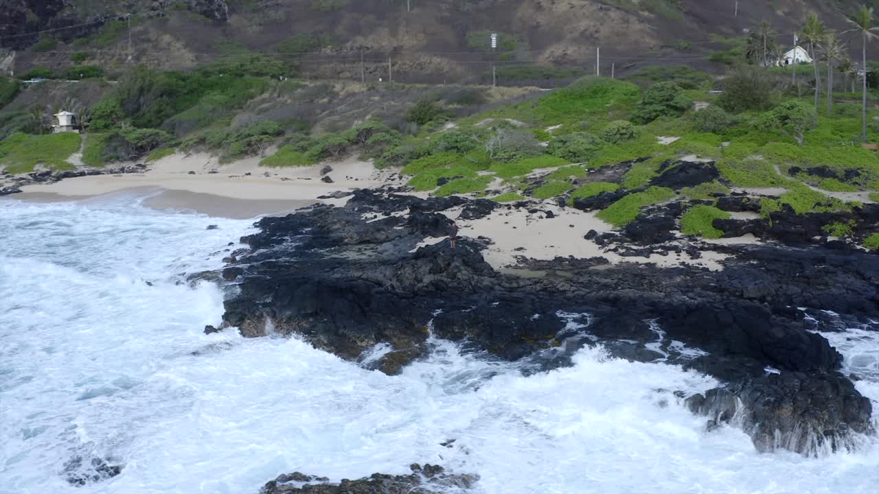 Man standing at Makapuu Oahu Hawaii rock outcropping as waves crash